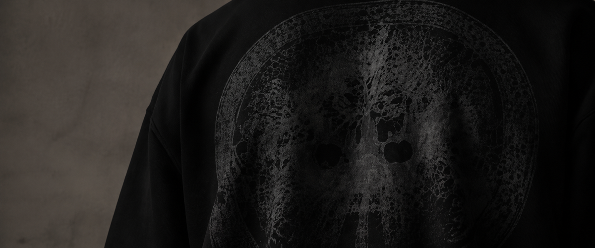 Close-up of a black garment featuring a large distressed circular graphic in dark gray tones on the back.