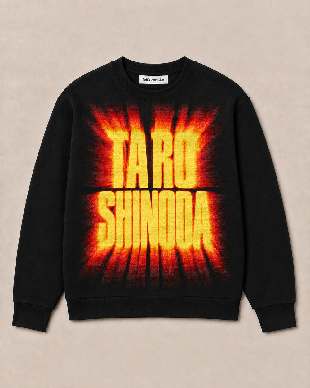 A black crewneck sweatshirt featuring a large graphic print of the name 'TARO SHINODA' in bold yellow letters with a red and orange flame-like burst background, displayed flat against a light beige textured backdrop.