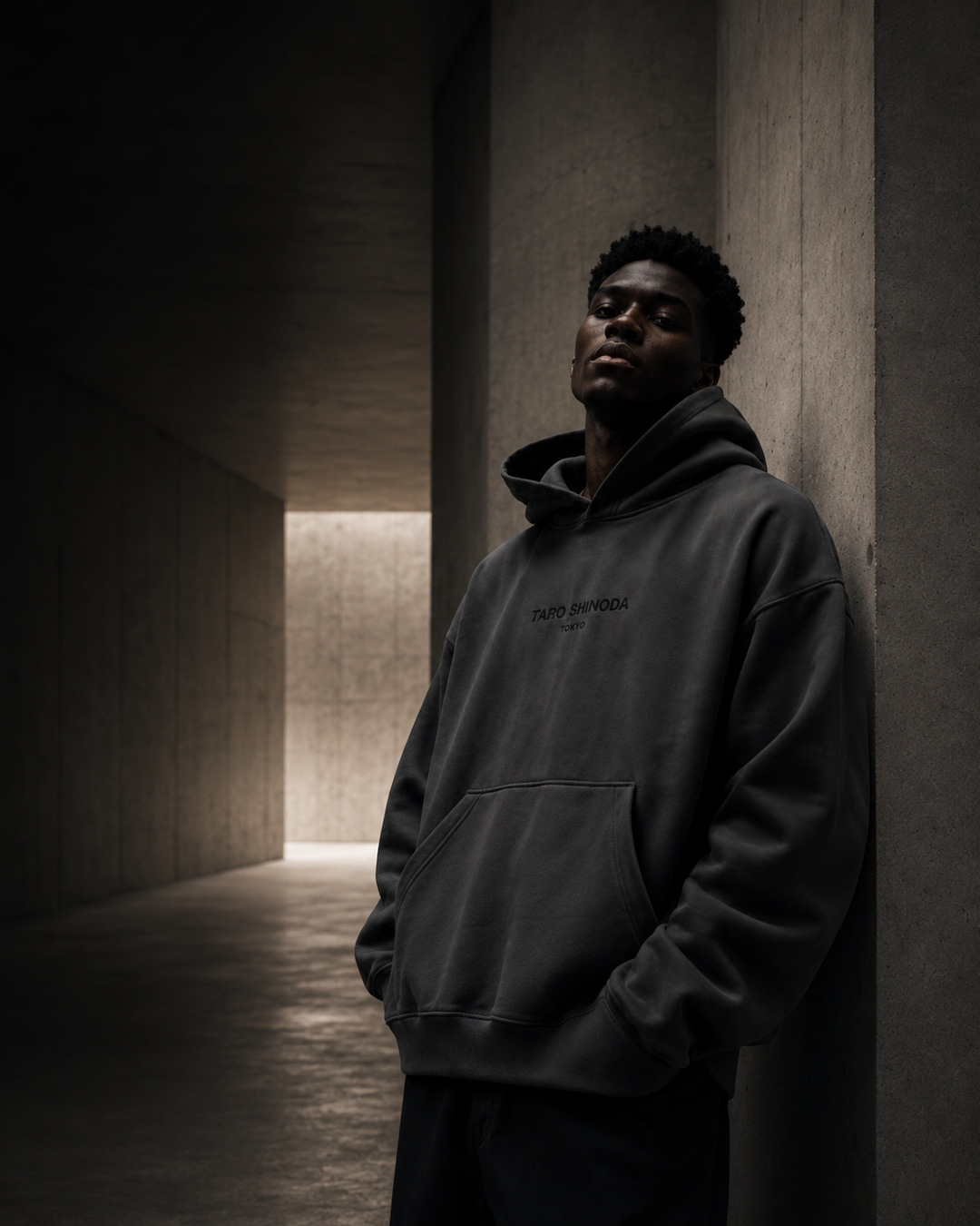 A man wearing a dark charcoal gray hoodie with 'SOUTH ENDOW' printed on the chest, leaning against a concrete wall in a dimly lit corridor.